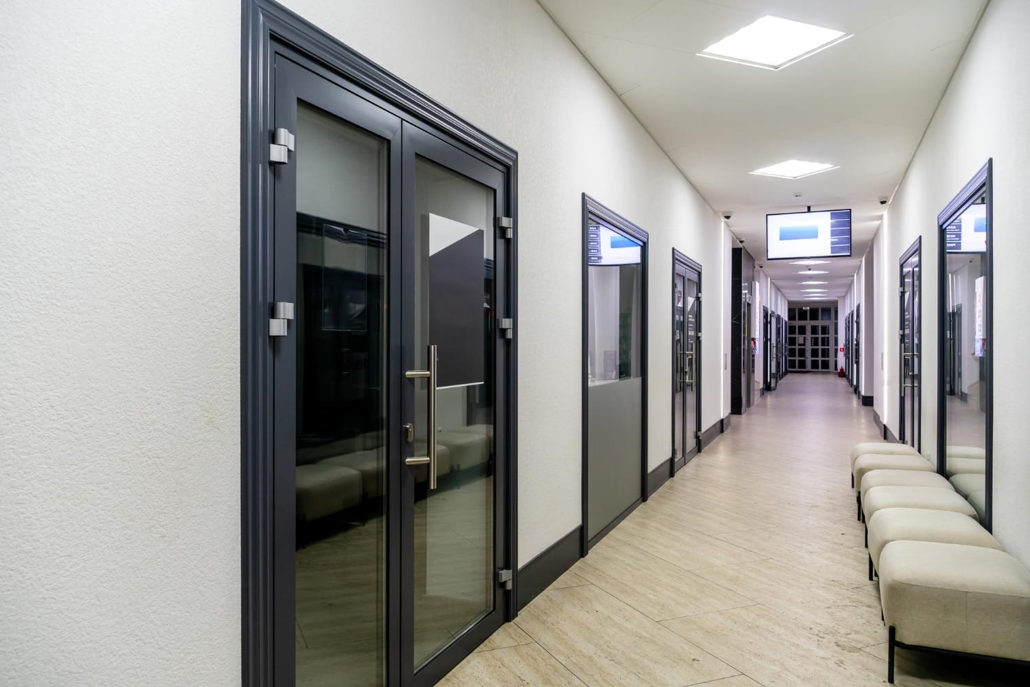 Office corridor with dark-framed glass doors and upholstered benches